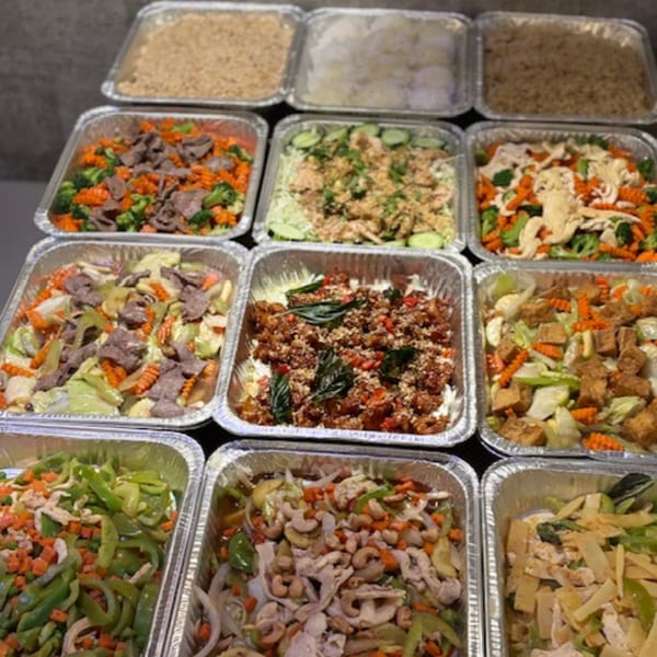Nine foil trays filled with various Asian dishes, including stir-fries, rice, and noodles.