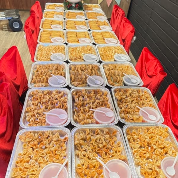 A long table covered in red cloth, laden with aluminum trays of golden fried appetizers and dipping sauces.