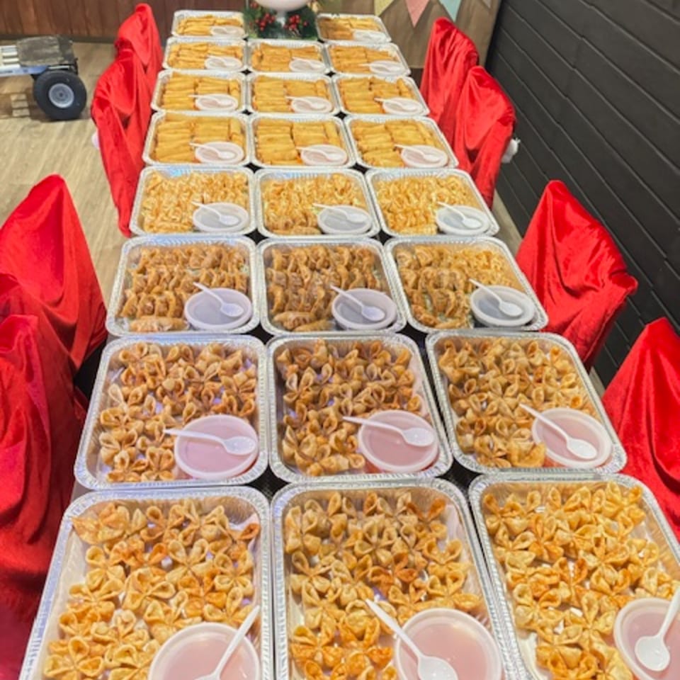 A long table covered in red cloth, laden with aluminum trays of golden fried appetizers and dipping sauces.