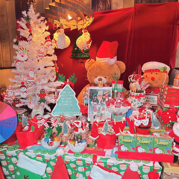 A festive Christmas display features a white tree, teddy bear, gingerbread man, and various candies.