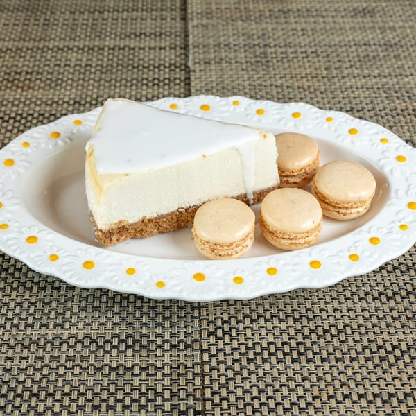 A slice of cheesecake with white icing and four macarons on a daisy-patterned plate.