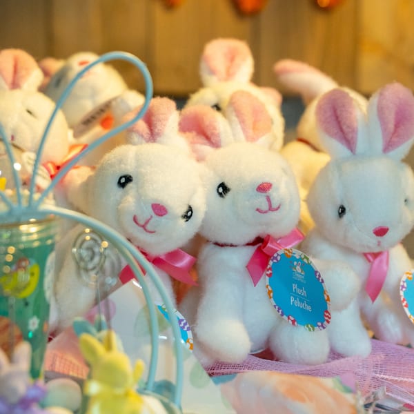 Several white plush bunny toys with pink ears and bows, some with "Plush" tags, in a display.
