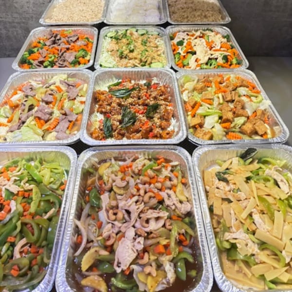 Assortment of Thai dishes in aluminum catering trays, including rice, stir-fries, and curries.