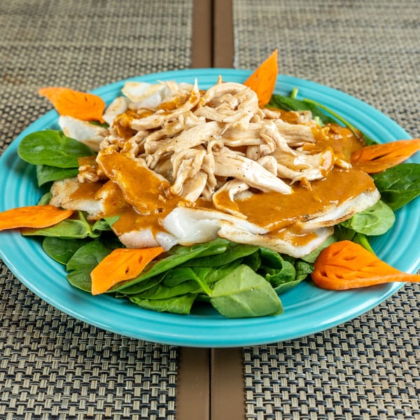 Chicken and spinach salad with orange dressing and carrot garnishes on a blue plate.