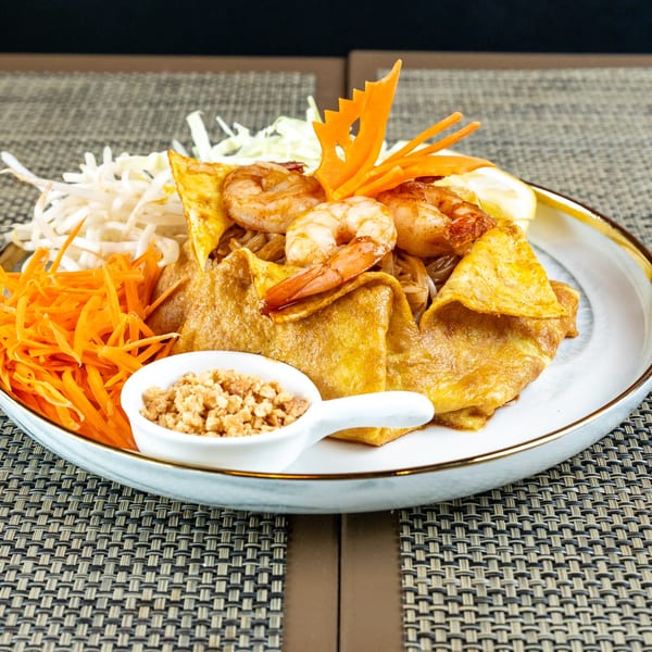 Pad Thai with shrimp, egg, shredded carrots, bean sprouts, and crushed peanuts on a white plate.