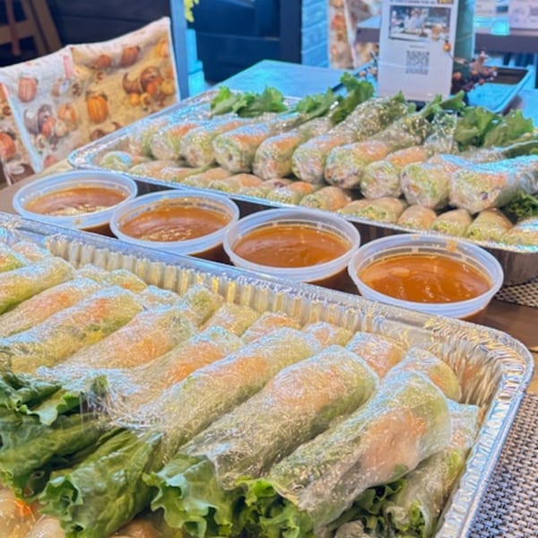 Two foil trays filled with fresh spring rolls and small containers of dipping sauce.