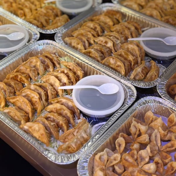 Several foil trays filled with golden-brown fried dumplings and small containers of dipping sauce.