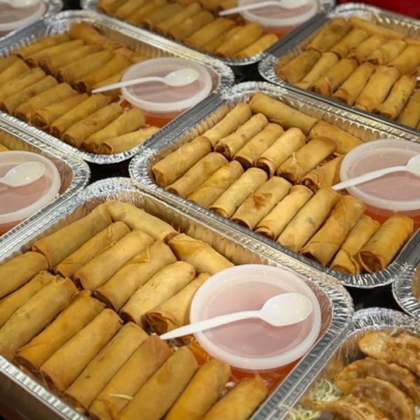 Multiple foil trays filled with golden-brown spring rolls and small containers of dipping sauce.