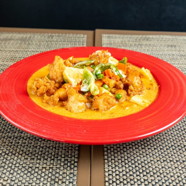 Crispy chicken and vegetables in a rich yellow curry sauce, served on a vibrant red plate.