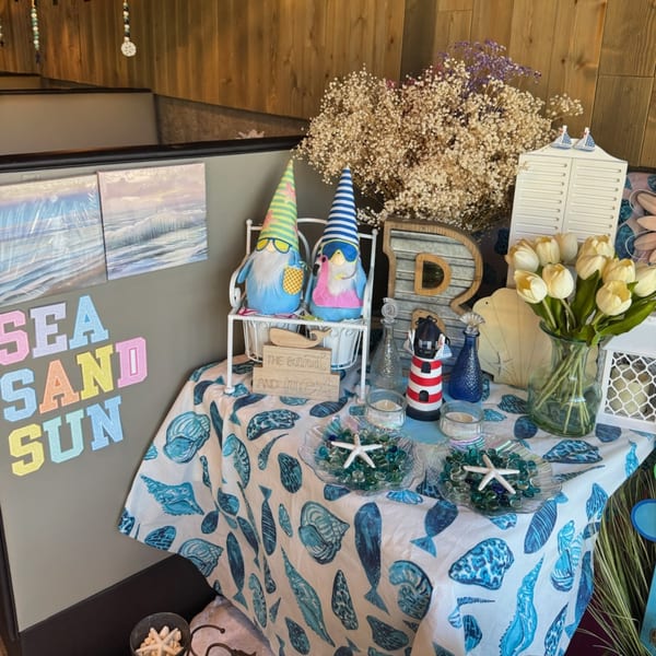 A table decorated with beach-themed items, including gnomes, seashells, a lighthouse, and tulips.