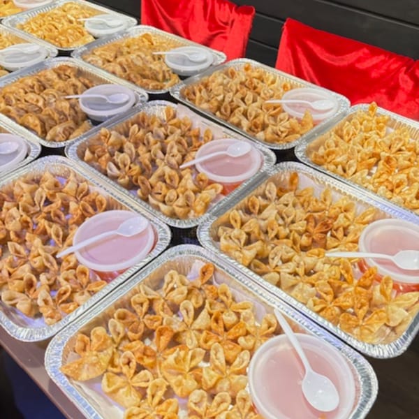 Numerous foil trays filled with golden-brown crab rangoons and small containers of pink dipping sauce.