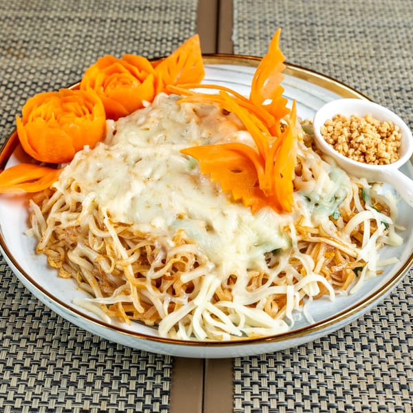 Noodles with melted cheese, garnished with carved carrots and a side of crushed peanuts.