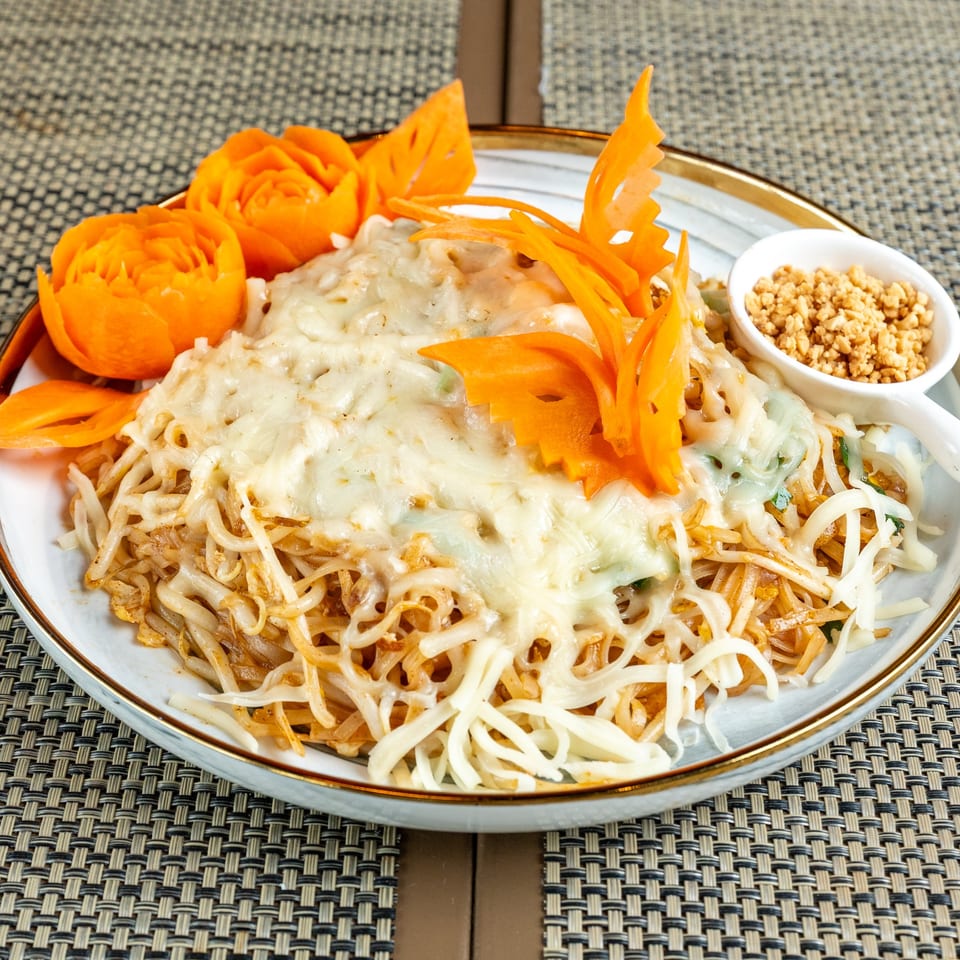 Noodles with melted cheese, garnished with carved carrots and a side of crushed peanuts.