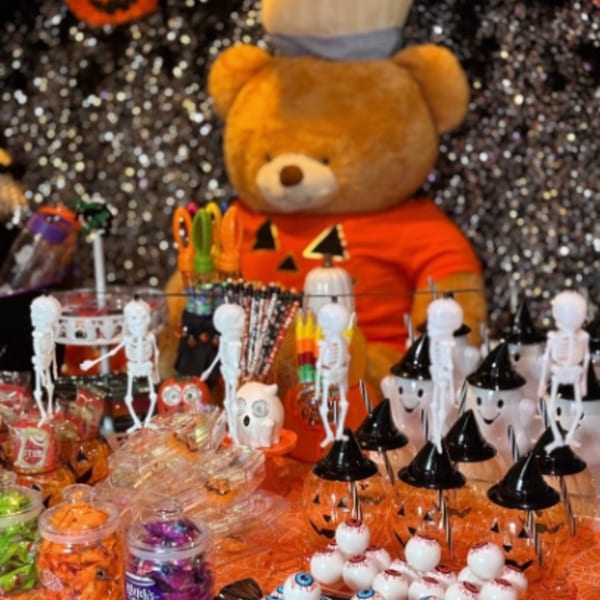 A Halloween candy display with a large teddy bear, skeletons, ghosts, and pumpkin-themed treats.